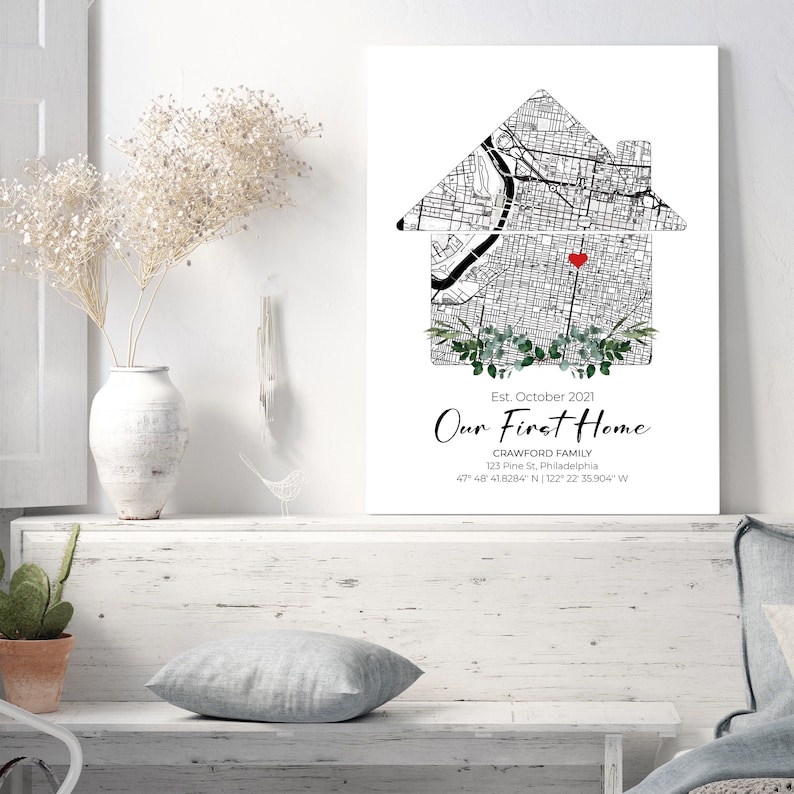 Puede incluir: Una ilustraci&oacute;n en blanco y negro de una casa con un coraz&oacute;n rojo en el centro, rodeada de vegetaci&oacute;n. El texto "Our First Home" est&aacute; debajo de la casa, junto con el nombre de la familia, la direcci&oacute;n y las coordenadas. El fondo es blanco.