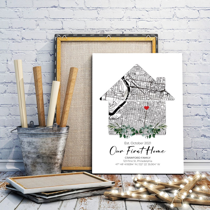 Puede incluir: Un mapa en blanco y negro de una ciudad est&aacute; impreso en forma de casa con un coraz&oacute;n rojo en el centro. El texto "Est. octubre 2021 Nuestro primer hogar Crawford Family 123 Pine St, Filadelfia 47&deg; 48 41.8284" N 122&deg; 22 35.904" W" est&aacute; impreso debajo de la casa.