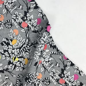 May include: Fabric with a repeating pattern of lemurs, trees, and fruit in black, white, and various colors. The fruit is in shades of pink, orange, yellow, and green. The lemurs are gray and white.