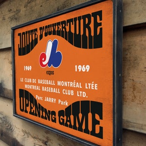 May include: A vintage-style wooden sign with black lettering and a Montreal Expos logo. The sign reads "JOUTE D'OUVERTURE 1969 Expos 1969 LE CLUB DE BASEBALL MONTR&Eacute;AL LT&Eacute;E MONTREAL BASEBALL CLUB LTD. Parc JARRY Park OPENING GAME".