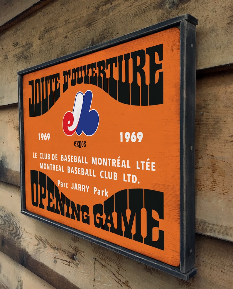 May include: A vintage-style wooden sign with black lettering and a Montreal Expos logo. The sign reads "JOUTE D'OUVERTURE 1969 Expos 1969 LE CLUB DE BASEBALL MONTR&Eacute;AL LT&Eacute;E MONTREAL BASEBALL CLUB LTD. Parc JARRY Park OPENING GAME".