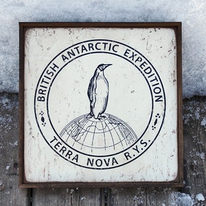 May include: A white sign with a black and white illustration of a penguin standing on a globe. The sign reads "British Antarctic Expedition Terra Nova R.Y.S."