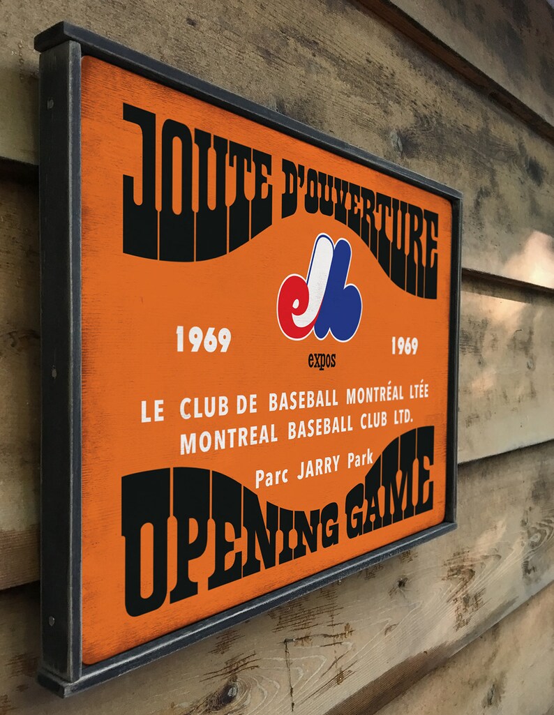 May include: A vintage-style wooden sign with a black frame and orange background. The sign reads "JOUTE D'OUVERTURE" in a retro font, with the Montreal Expos logo and the years 1969. The text below reads "LE CLUB DE BASEBALL MONTR&Eacute;AL LT&Eacute;E MONTREAL BASEBALL CLUB LTD. Parc JARRY Park OPENING GAME".