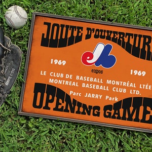 May include: A vintage-style wooden sign with an orange background and black text. The sign reads "JOUTE D'OUVERTURE 1969 LE CLUB DE BASEBALL MONTREAL BASEBALL CLUB LTD. Parc JARRY Park OPENING GAME". The sign also features a baseball logo with the word "expos" underneath.