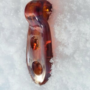 May include: A brown glass bottle stopper with two holes. The stopper is sitting on a bed of white snow.