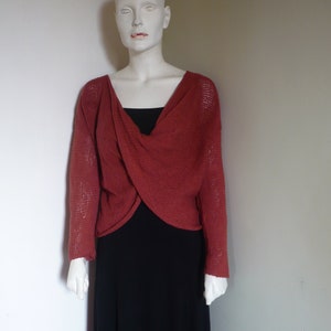 Puede incluir: Un maniquí exhibe un suéter de manga larga color óxido sobre un vestido negro. El suéter tiene un diseño envolvente único. El vestido es de estilo maxi con un dobladillo asimétrico. El maniquí es blanco.