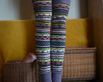 May include: A pair of colorful knitted leg warmers with a geometric pattern in shades of blue, green, pink, and purple. The leg warmers are displayed on a mannequin, showcasing their design and fit. The leg warmers are a cozy accessory.