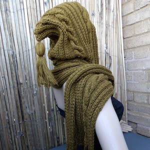 May include: A brown knitted hooded scarf with long tassels. The scarf is made of a thick yarn and has a cable knit pattern.
