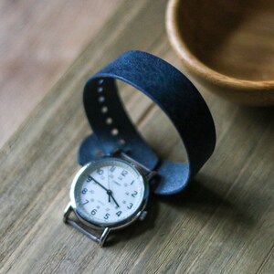 May include: A silver wristwatch with a white face and black hands. The watch has a dark blue leather band.