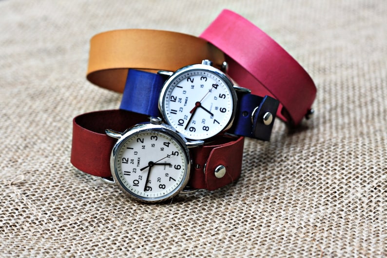 May include: Three wristwatches with white faces and black hands, each with a different colored leather band: red, blue, and brown.