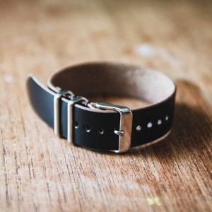 May include: A black leather watch strap with silver buckle and keepers.