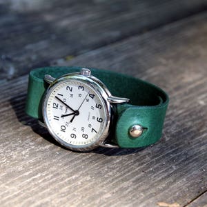 May include: A silver wristwatch with a white face and black hands on a dark green leather band.