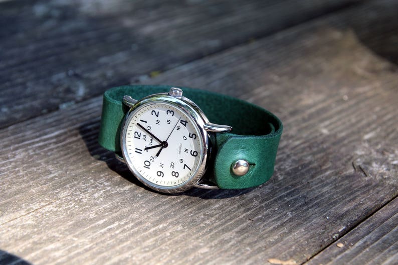 May include: A silver wristwatch with a white face and black hands on a dark green leather band.