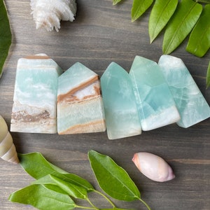 May include: Five teal blue and brown banded agate crystal points arranged in a row on a wooden surface. The points are polished and have a smooth, glassy finish.