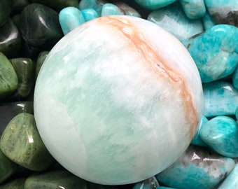 May include: A smooth, light green and white sphere with a brown stripe. The sphere is surrounded by smaller, teal green stones.