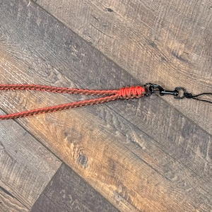 May include: A brown and orange braided lanyard with a black metal swivel clip and a black string loop.