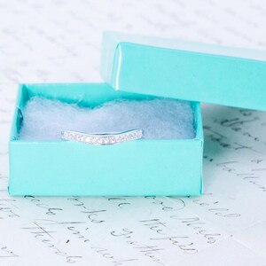 May include: A silver ring with small diamonds set in a curved band, displayed in a light blue gift box.