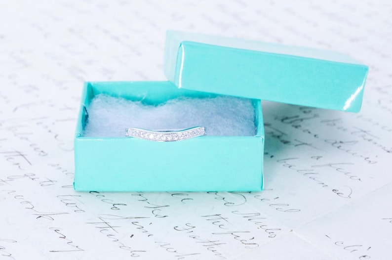 May include: A silver ring with small diamonds set in a curved band, displayed in a light blue gift box.
