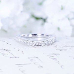 May include: A delicate, curved wedding band with a row of small, sparkling diamonds set in a silver band.