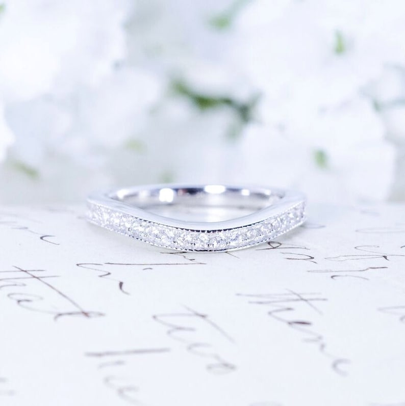 May include: A delicate, curved wedding band with a row of small, sparkling diamonds set in a silver band.