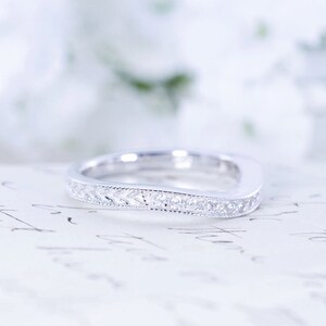 May include: A delicate, curved wedding band with a sparkling diamond-encrusted design. The band is made of white metal and is set against a white background.