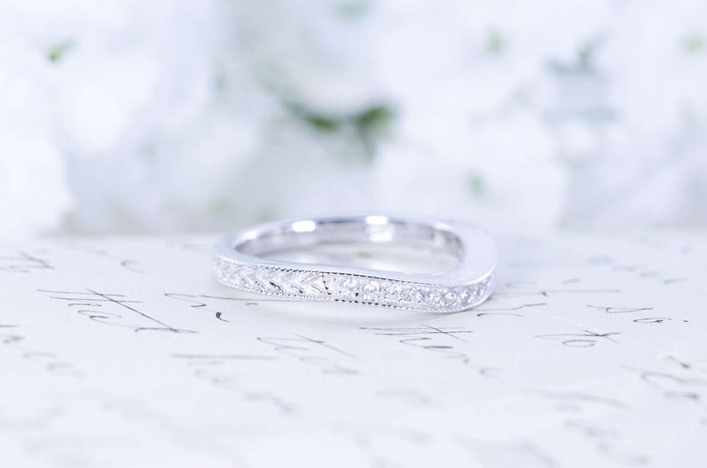 May include: A delicate, curved wedding band with a sparkling diamond-encrusted design. The band is made of white metal and is set against a white background.