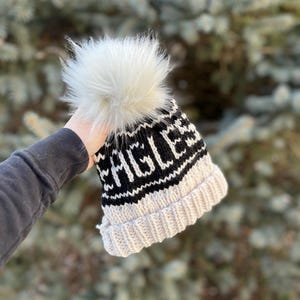 May include: A white and black knit beanie with a white pom pom and the word "EAGLE" in black lettering.