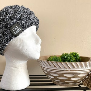 Hand Cabled And Knitted Cat Lady Ear Warmer For Women With Black Faux Leather Label, Dark Grey And White Flecked Winter Accessory