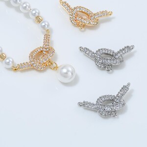 May include: A pearl necklace with a gold-toned knot pendant, adorned with clear crystals and a dangling pearl. Two additional knot-shaped pendants, one gold and one silver, are also visible.