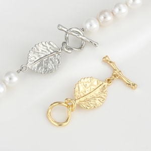 Könnte beinhalten: Eine Perlenkette mit einem Anhänger aus Silber und Gold in Blattform. Die Kette hat einen Toggle-Verschluss.