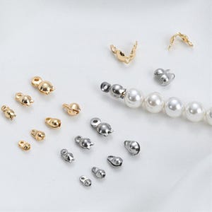 Può includere: Un assortimento di componenti per gioielli, tra cui terminali e chiusure dorate e argentate. Diverse perle sono infilate, mostrando i componenti utilizzati nella creazione di gioielli. I componenti variano in dimensioni e forma, adatti a vari design di gioielli.