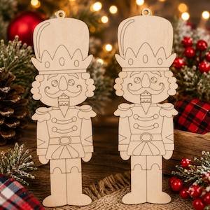 May include: Two light-colored wooden nutcracker ornaments featuring laser-cut outlines of a soldier in a tall hat, uniform jacket, and boots. Each flat wooden cutout includes a small circular hole at the top for hanging as a holiday decoration.