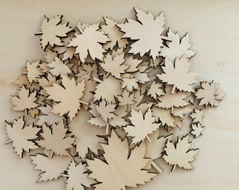 May include: A collection of numerous light-colored wooden maple leaf cutouts of varying sizes. Each piece features the distinct five-pointed shape of a maple leaf with a small stem at the base, arranged in a dense, overlapping cluster.