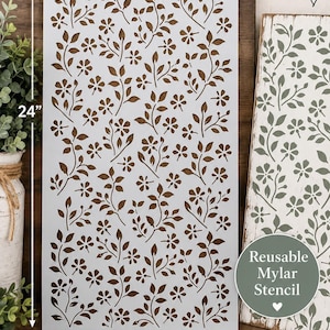 May include: A rectangular reusable Mylar stencil measuring 12 inches by 24 inches, featuring a repeating pattern of small flowers and leaves. The stencil is white with cutouts, shown alongside a wooden board with the same floral design painted on it.