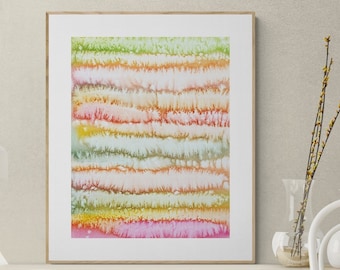 Puede incluir: Una impresión de arte abstracto enmarcada con rayas horizontales de rosa, naranja, amarillo, verde y azul. La impresión está colgada en una estantería de pared de madera clara con una lámpara blanca y una silla blanca con una manta blanca.