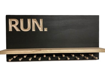 Può includere: Uno scaffale in legno nero con la parola "RUN." intagliata sul davanti. Lo scaffale ha una fila di pioli in legno per appendere oggetti.