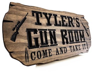 Può includere: Un cartello di legno con il testo "Tyler's Gun Room Come and Take It" in lettere nere. Il cartello presenta due fucili e due proiettili su entrambi i lati del testo.