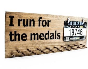 Puede incluir: Expositor de medallas de madera con el texto "I run for the medals" y un dorsal de carrera con el texto "The Color Run Night 19746".