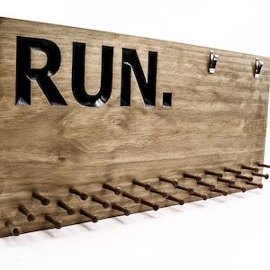 May include: A wooden medal display with the word "RUN." in black lettering. The display has 30 hooks for hanging medals.