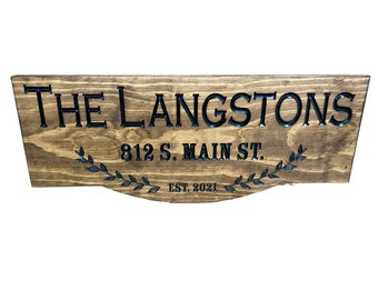 Può includere: Un cartello in legno con il testo "The Langstons 812 S. Main St. Est. 2021" in lettere nere. Il cartello ha una finitura in legno marrone e un motivo decorativo a foglie.