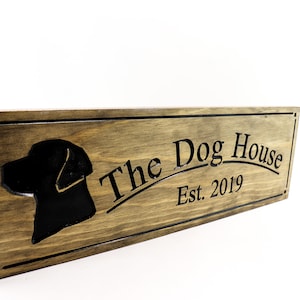 May include: A wooden sign with a black silhouette of a dog's head and the text "The Dog House Est. 2019" carved into the wood.