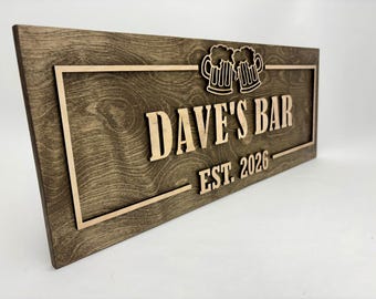 Può includere: Targa in legno rettangolare con la scritta "DAVE'S BAR EST. 2026" in rilievo. La targa è tinta di marrone scuro con un bordo marrone più chiaro e due boccali di birra. Il legno ha una trama a venature visibili.