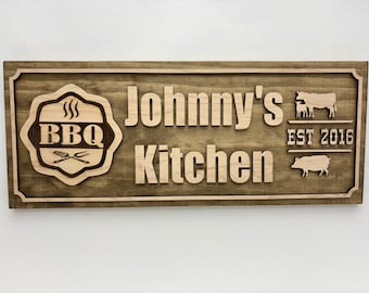 Può includere: Cartello in legno con le parole "Johnny's Kitchen" e "BBQ" in legno chiaro, su uno sfondo in legno tinto più scuro. Include una mucca, un maiale e il testo "EST 2016".