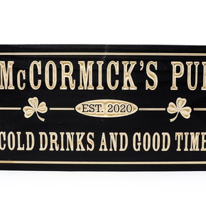 May include: Black wooden sign with gold lettering that reads "McCormick's Pub Est. 2020 Cold Drinks and Good Times". The sign has a shamrock design on either side of the text.
