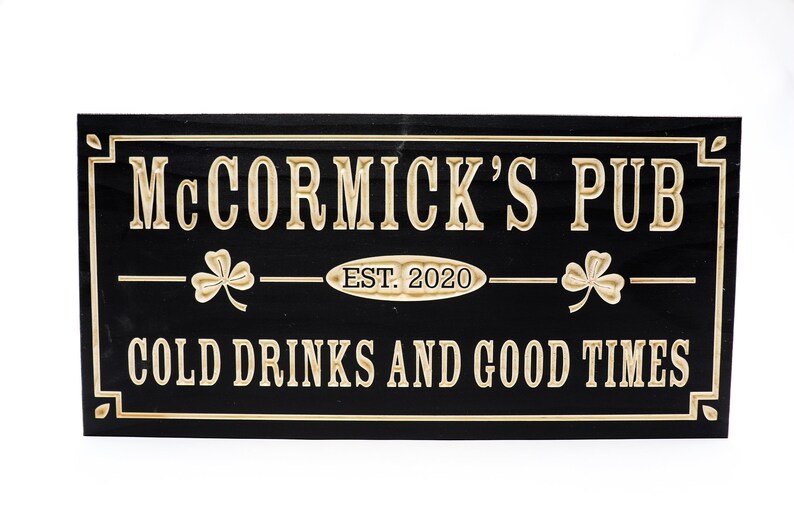 May include: Black wooden sign with gold lettering that reads "McCormick's Pub Est. 2020 Cold Drinks and Good Times". The sign has a shamrock design on either side of the text.