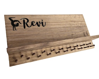 Può includere: Organizzatore da parete in legno con uno scaffale e ganci. L'organizzatore ha il nome "Revi" scritto su di esso e una silhouette di una ginnasta.