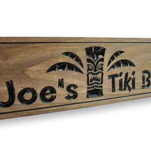 May include: A wooden sign with the text "Joe's Tiki Bar" carved into it. The sign features a tiki head and palm trees.