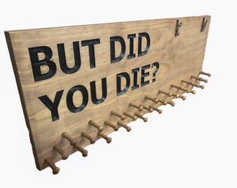 Può includere: Un porta medaglie in legno con la scritta "But Did You Die?" in lettere nere. Il porta medaglie ha 20 ganci per appendere le medaglie.