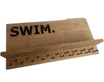 Può includere: Organizzatore da parete in legno con la scritta "SWIM" in lettere nere. L'organizzatore ha uno scaffale e una fila di pioli in legno.