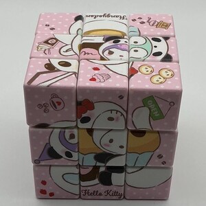 Puede incluir: Un rompecabezas de cubo rosa con temática de Hello Kitty con imágenes de Hello Kitty, un panda y tazas de café. El cubo tiene un patrón de lunares y las palabras "Hello Kitty" y "Strawberry Garden" están impresas en los lados.